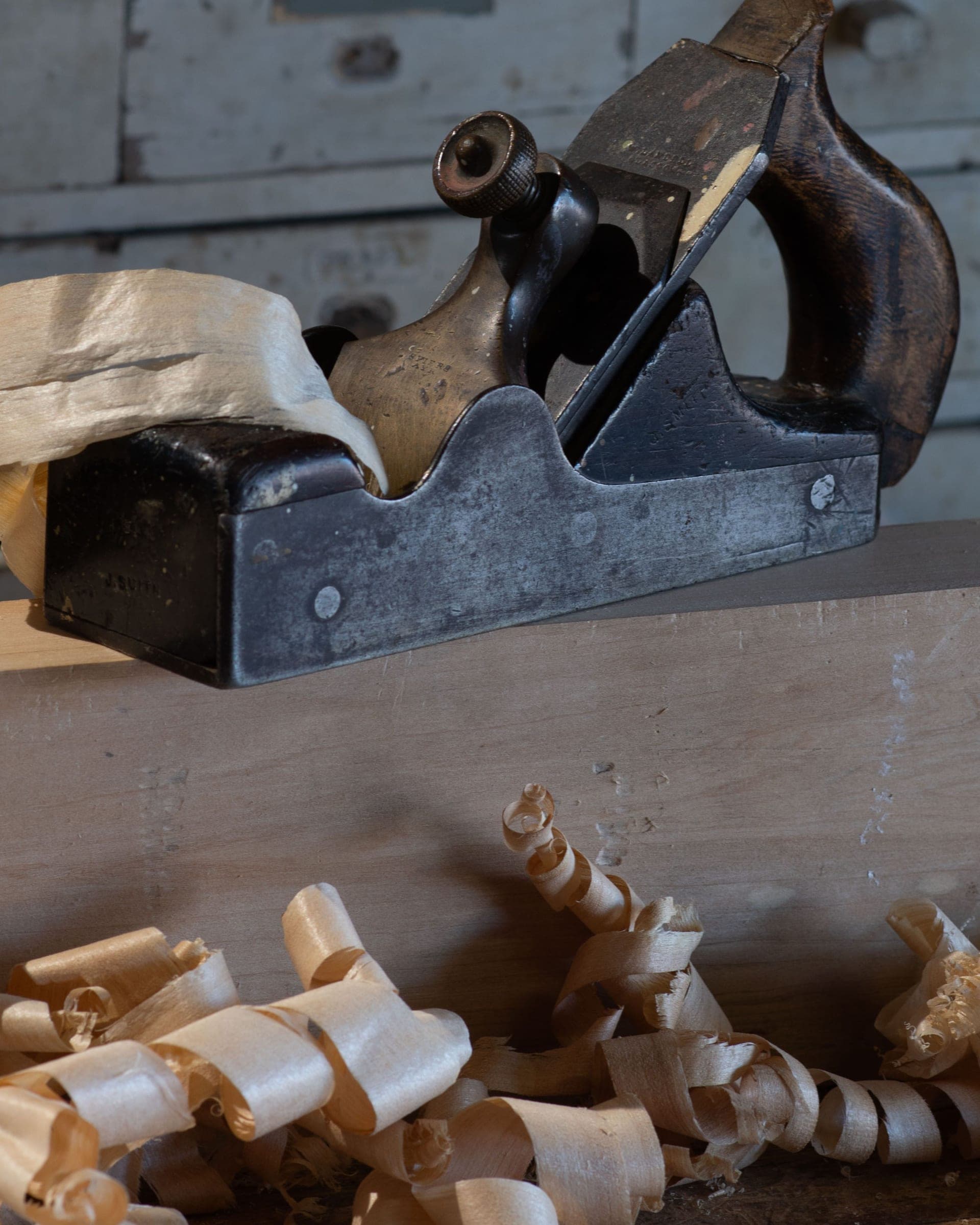 An old hand plane resting on a timber board among wood shavings